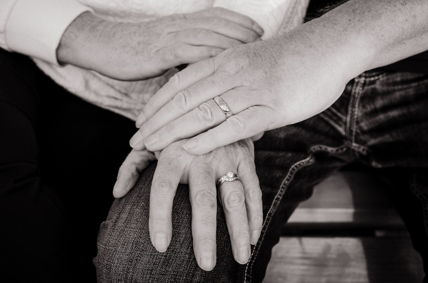 Black and white close-up of hands with wedding rings resting on lap.