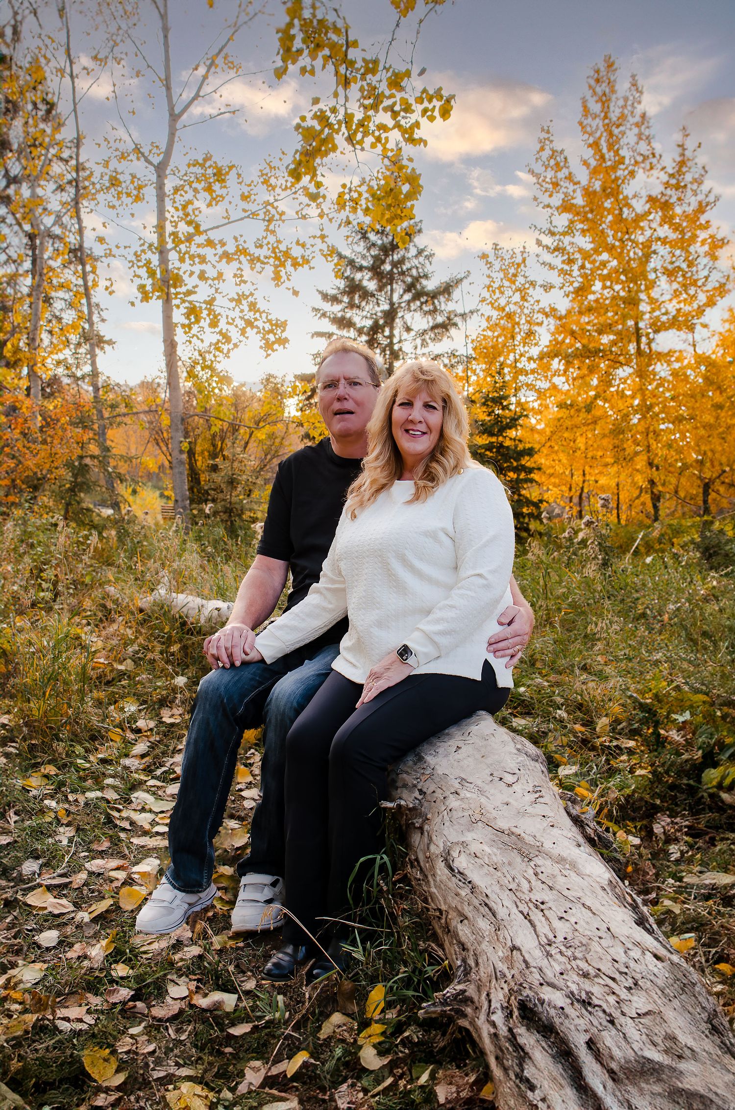 Couple sitting on fallen log surrounded by golden autumn trees.