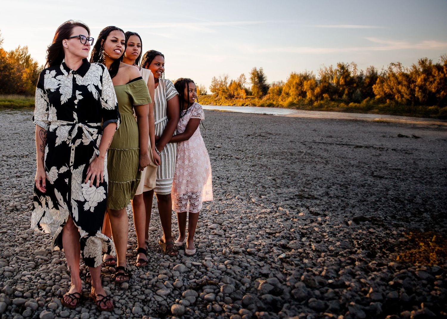 A group stands together on a rocky shoreline during golden hour with autumn trees in the background.