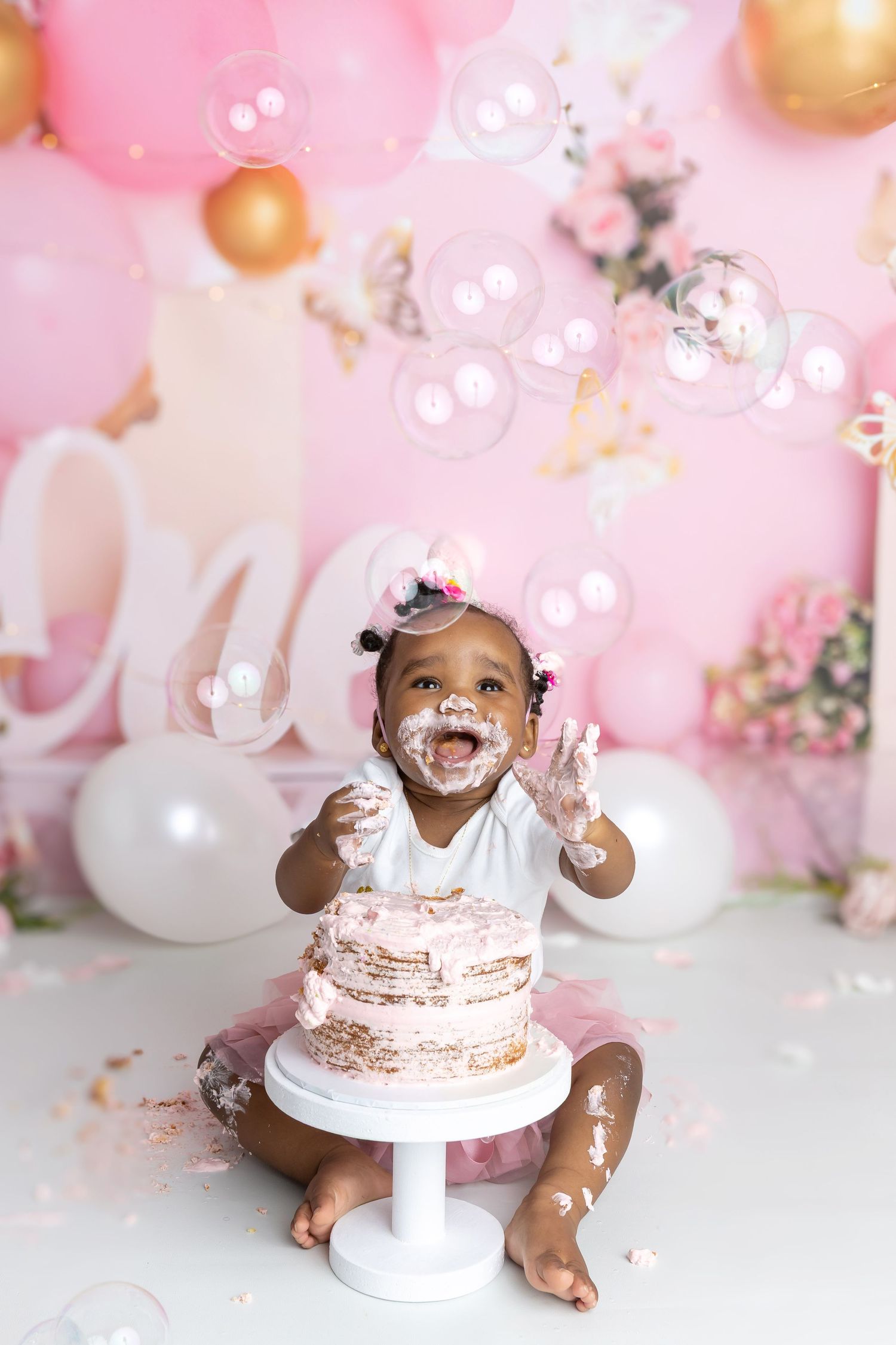 Image of little girl smiling and trying to catch bubbles at her cake smash photography session, cake smash & splash.