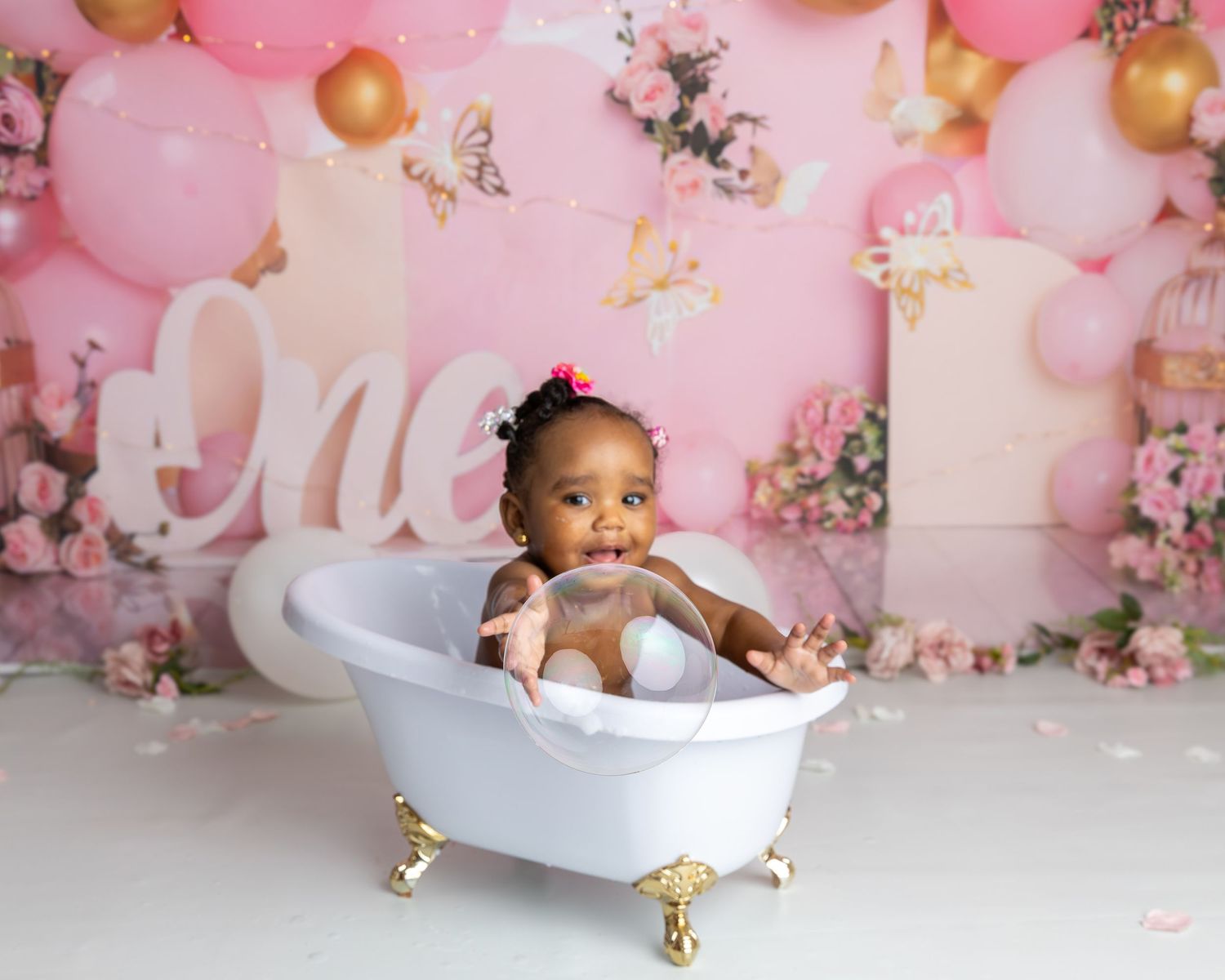 Photograph of little girl smiling having fun catching bubbles in the bath at her cake smash photography session, cake smash & splash.