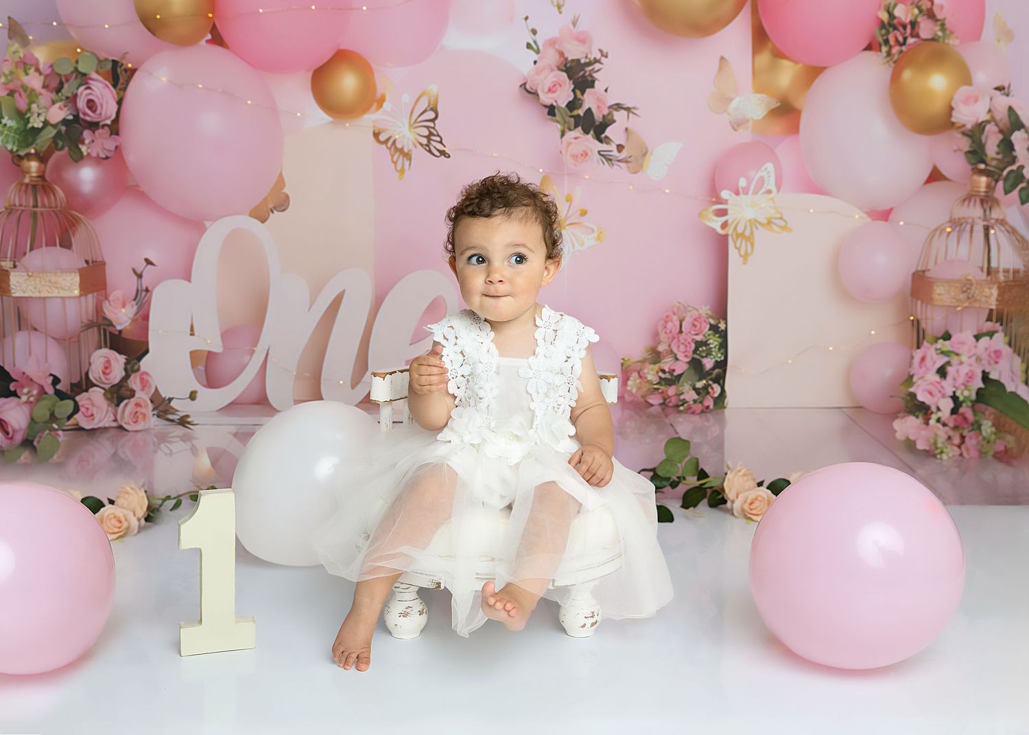 Image of little girl sitting in a chair wearing a white dress on set of her cake smash & splash with Shelly Loxton Photography