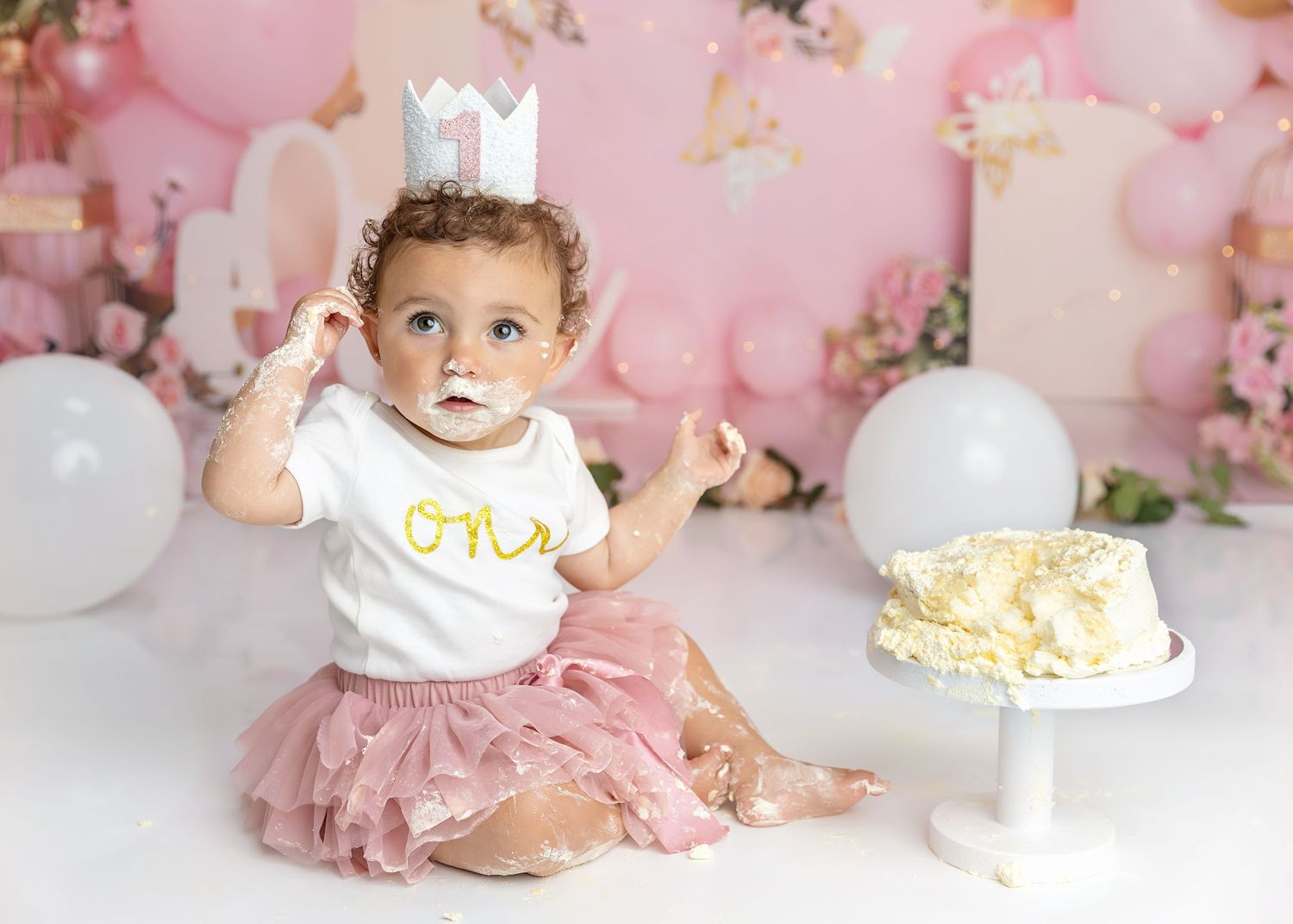 Photograph of little girl playing with her party hat at her cake smash photography session, cake smash & splash.