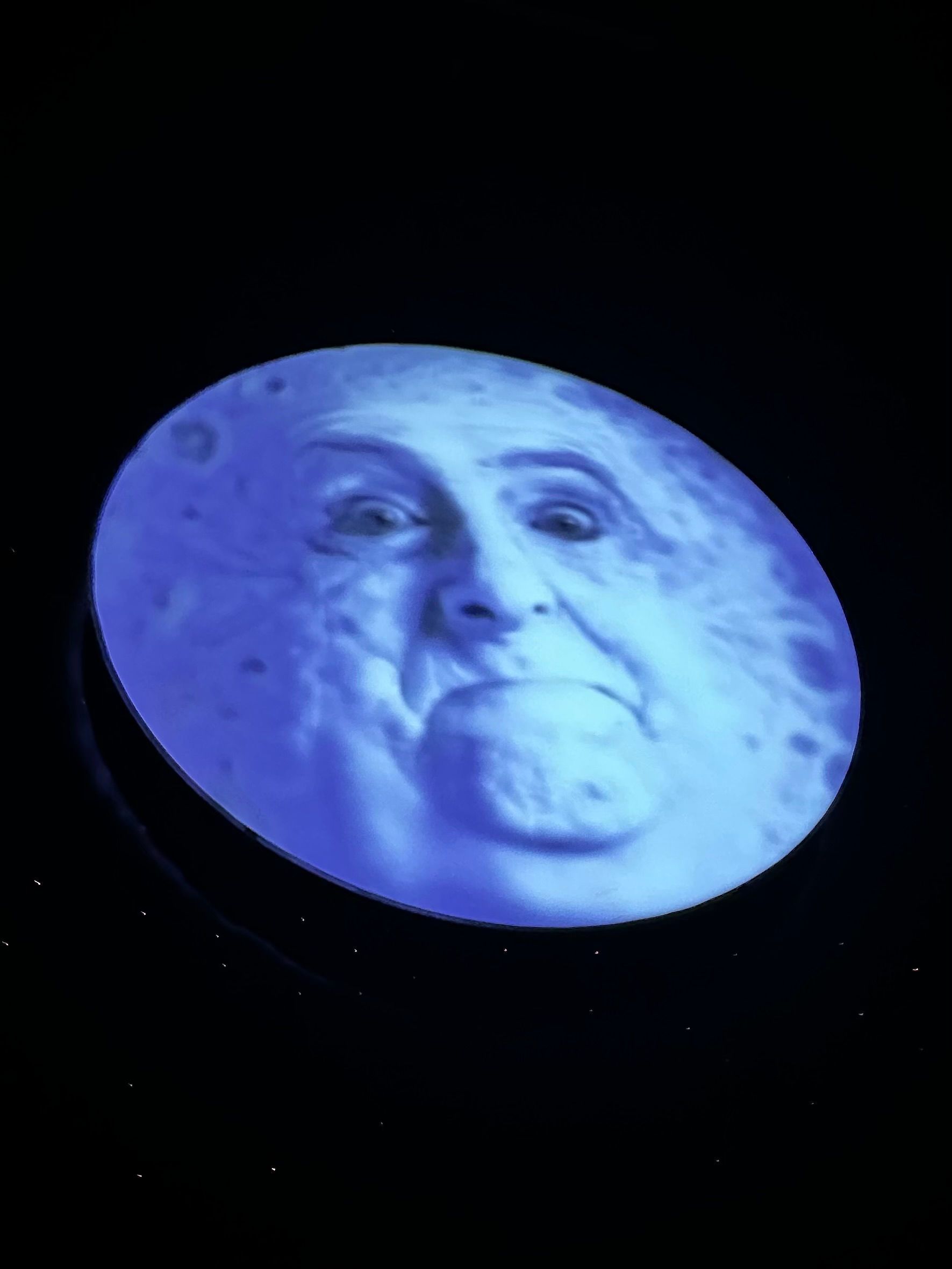 A circular projection shows a glowing blue face against a dark background with dramatic lighting and shadows.