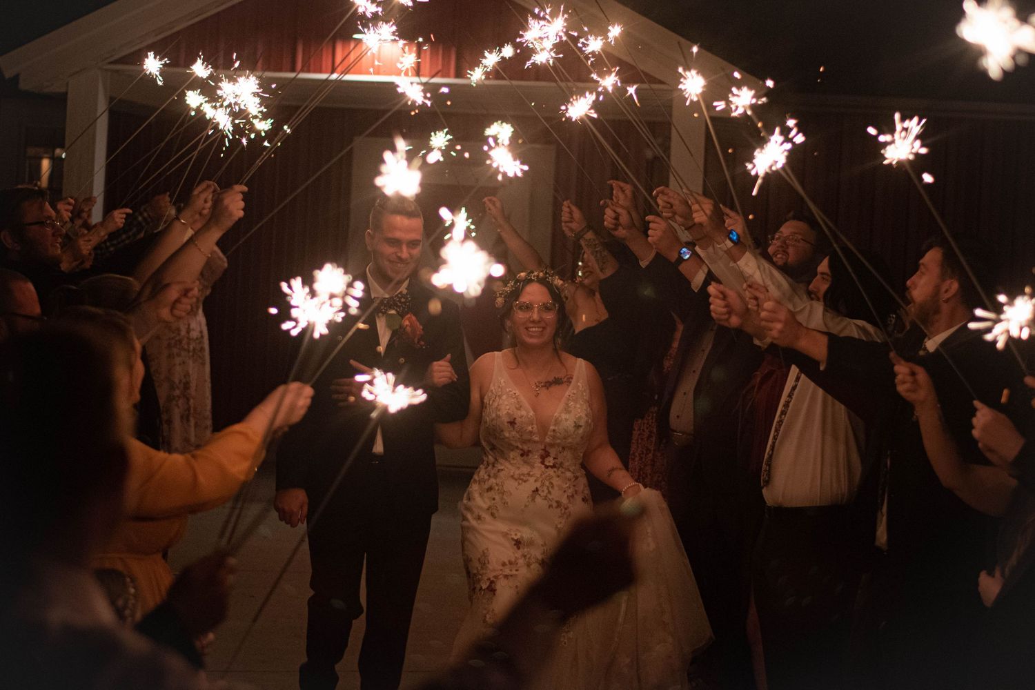 Wedding celebration at night with guests holding sparklers creating a magical tunnel of light.