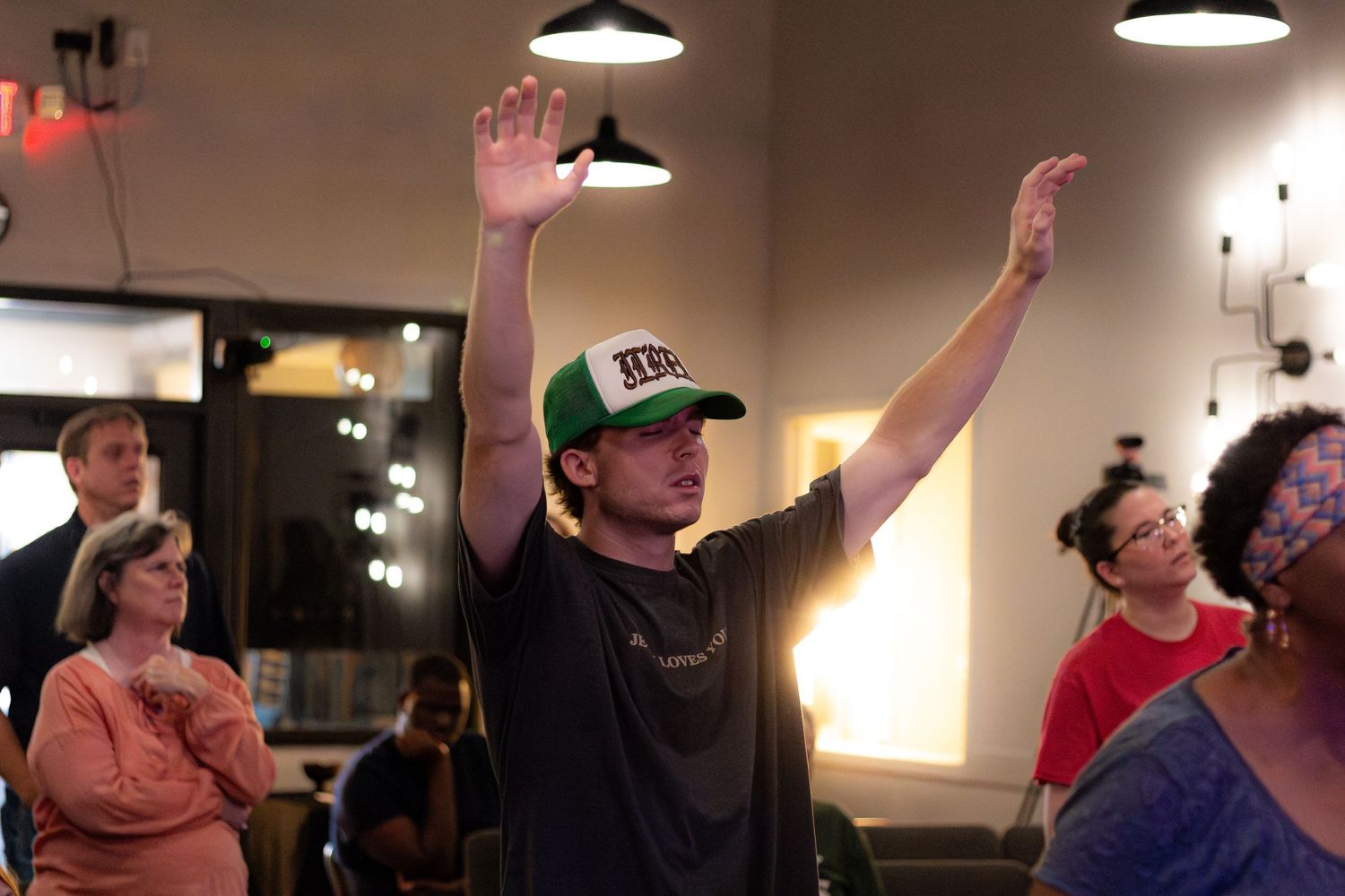 People enjoying themselves during a lively gathering indoors, with raised hands and bright lighting in the background.