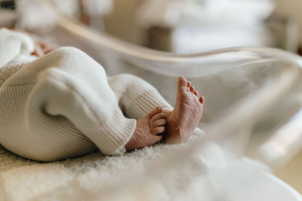A close-up view of tiny baby feet peeking out from under a white knit blanket.