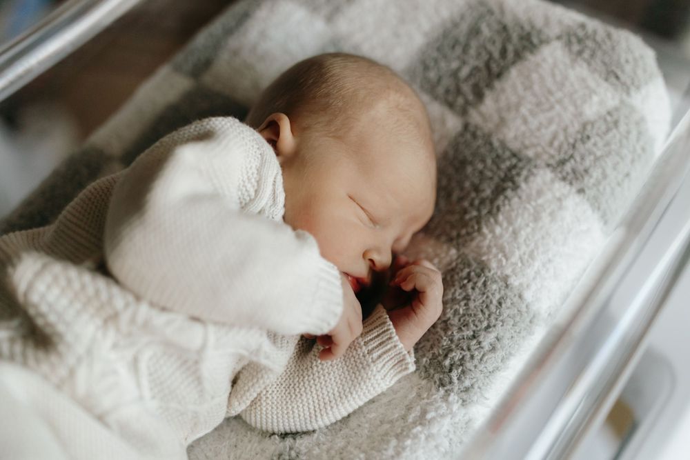 Peaceful newborn sleeping in clear hospital bassinet with white blanket.