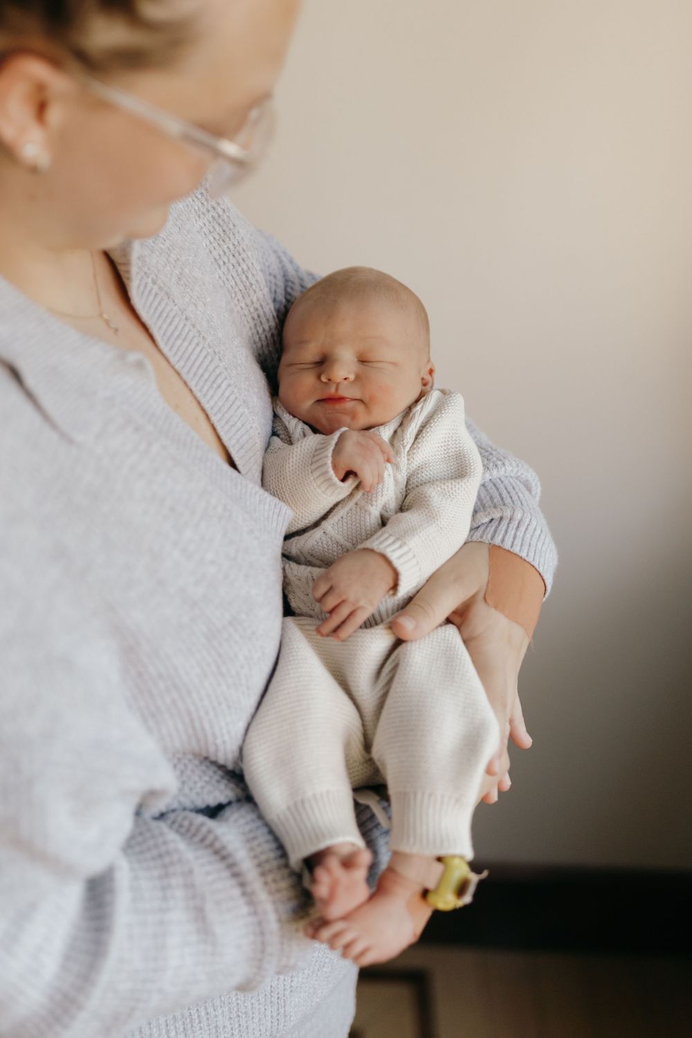Baby in white knit outfit being cradled in gray sweater.