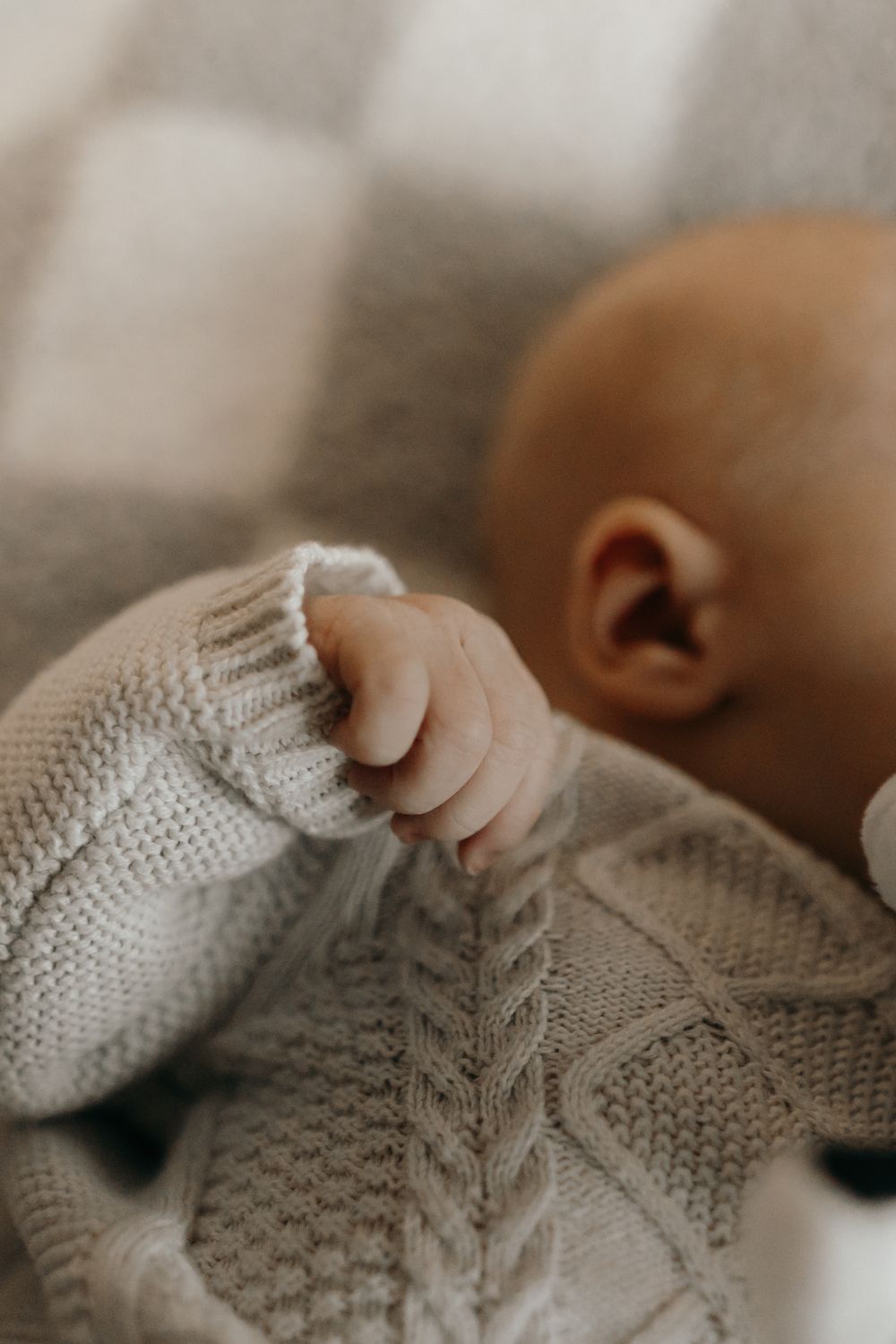 Close-up of tiny baby hand grasping cable knit white sweater.