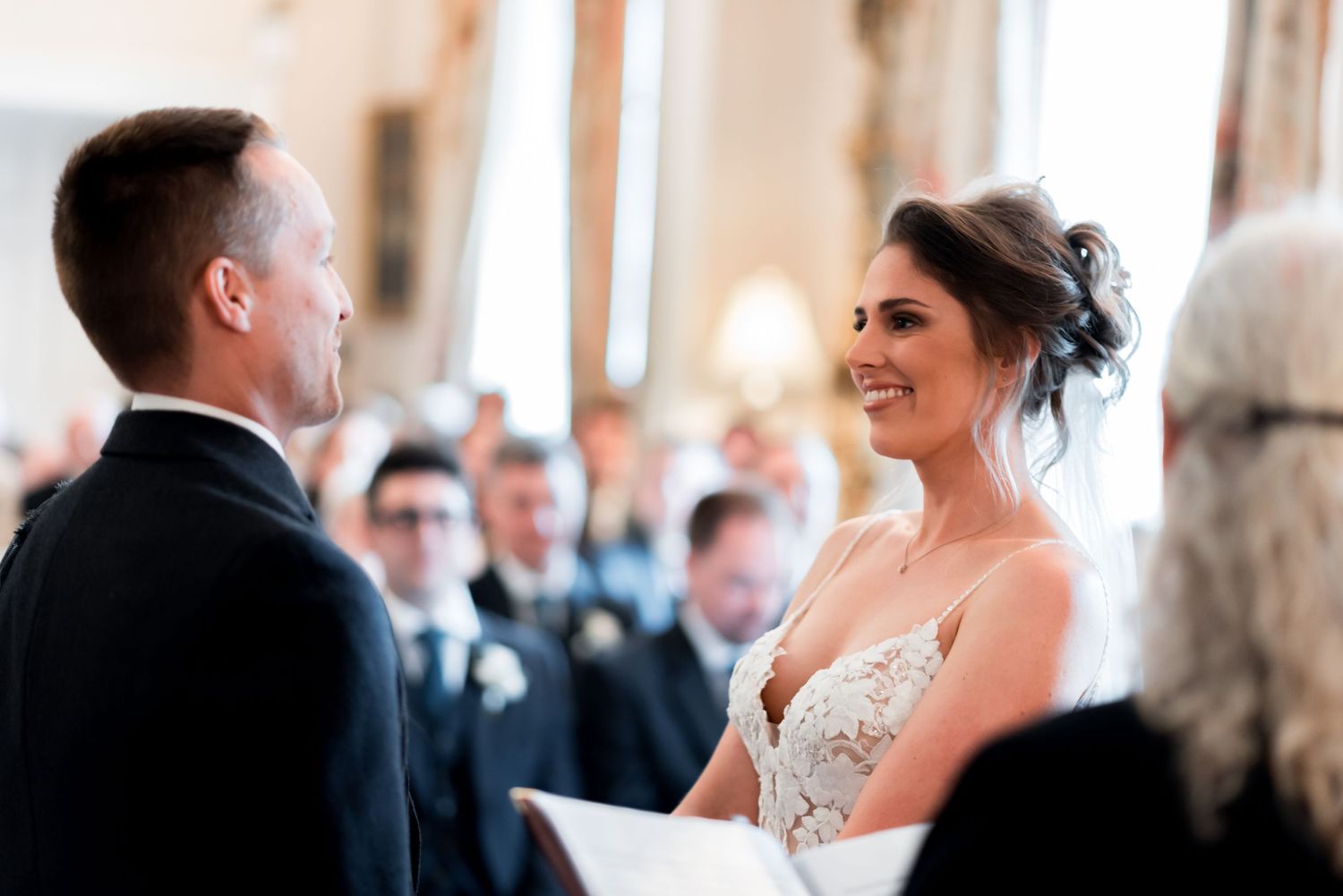 A happy couple exchanging vows during their wedding ceremony with guests watching in the background.