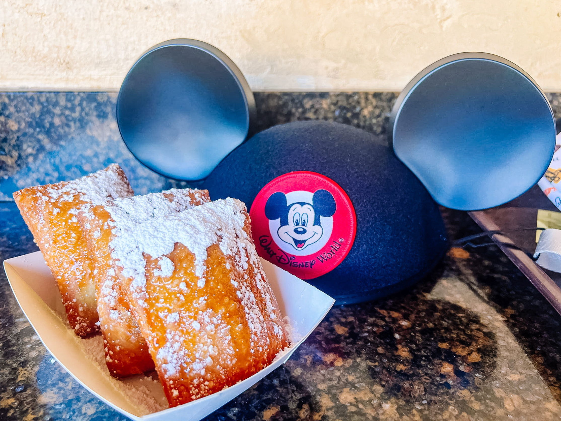 Mickey Mouse sunglasses sit atop powdered sugar dusted croissants on a black marble counter at Disney World.