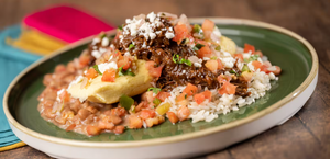 A colorful Mexican dish featuring grilled avocado, rice, salmon, and fresh pico de gallo served on a green plate.