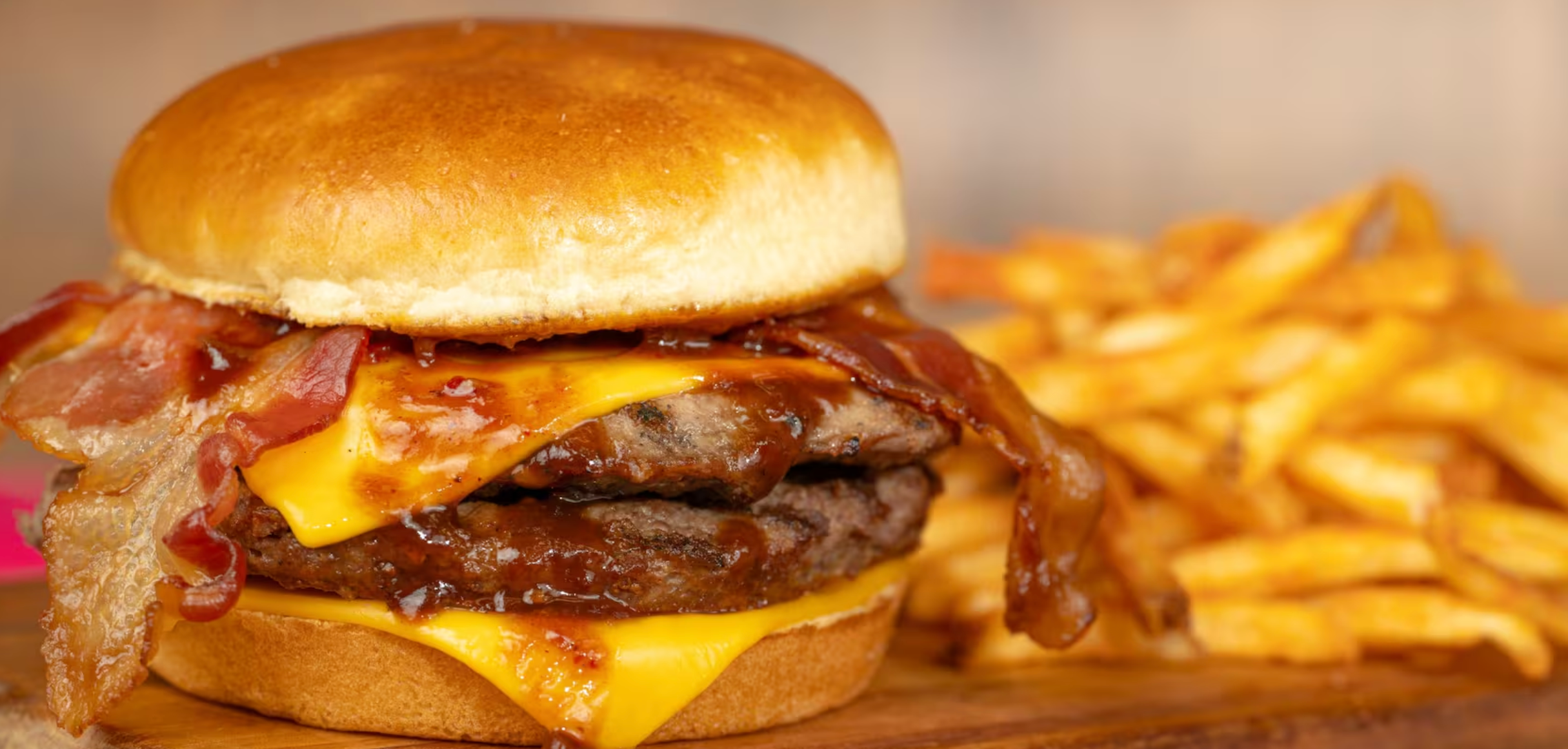 Juicy bacon cheeseburger with melted cheese on a golden bun served alongside crispy french fries on wooden board.