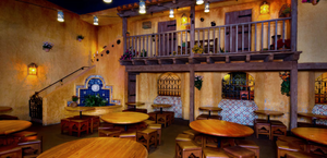 Rustic Mexican restaurant interior with wooden tables, balcony seating, and warm yellow lighting creating cozy ambiance.