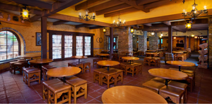 Rustic restaurant interior with wooden tables, arched windows, and warm lighting under exposed beam ceilings.