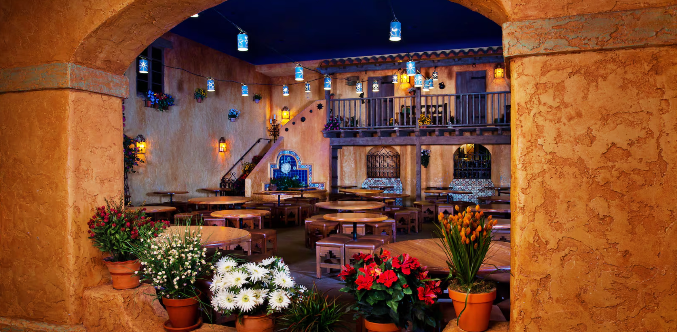 Mediterranean patio dining area with rustic stone columns, warm lighting, and mixed floral arrangements creating an inviting ambiance.
