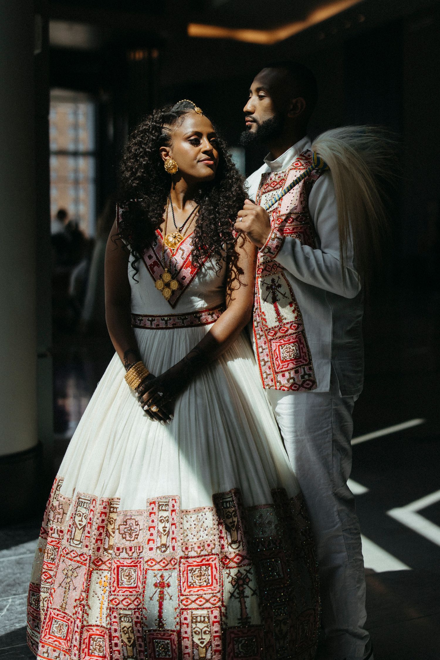 A couple in coordinating gray and red formal attire share a romantic moment together in a dimly lit indoor setting.