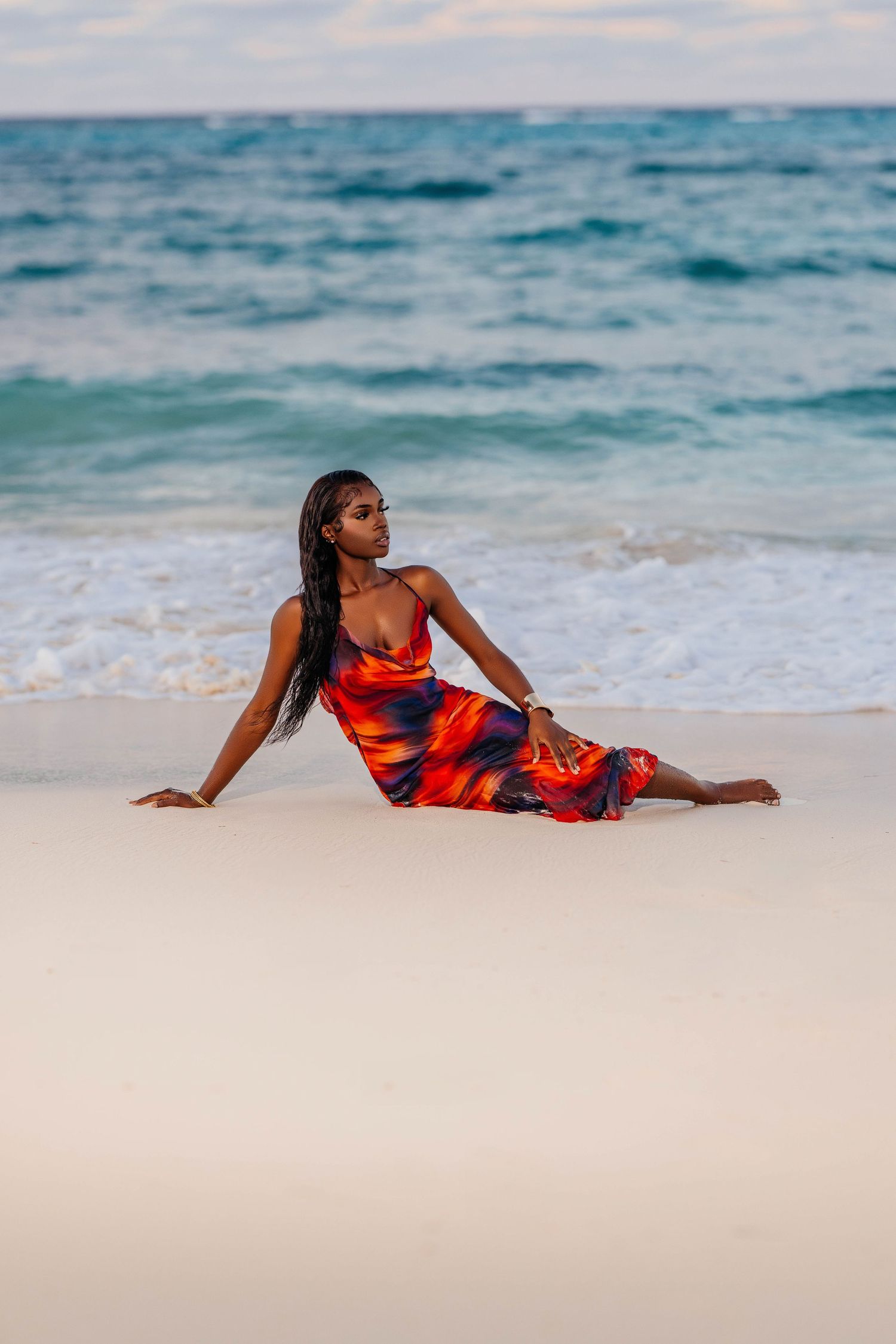 Woman in red and navy dress reclines elegantly on white sandy beach.