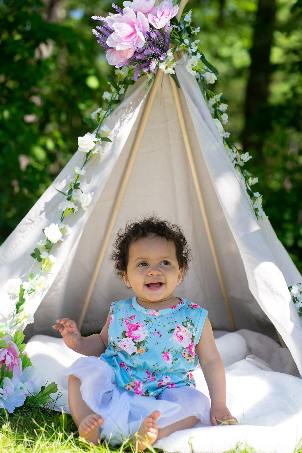Decorated teepee tent with floral accents and white fabric in an outdoor garden setting.