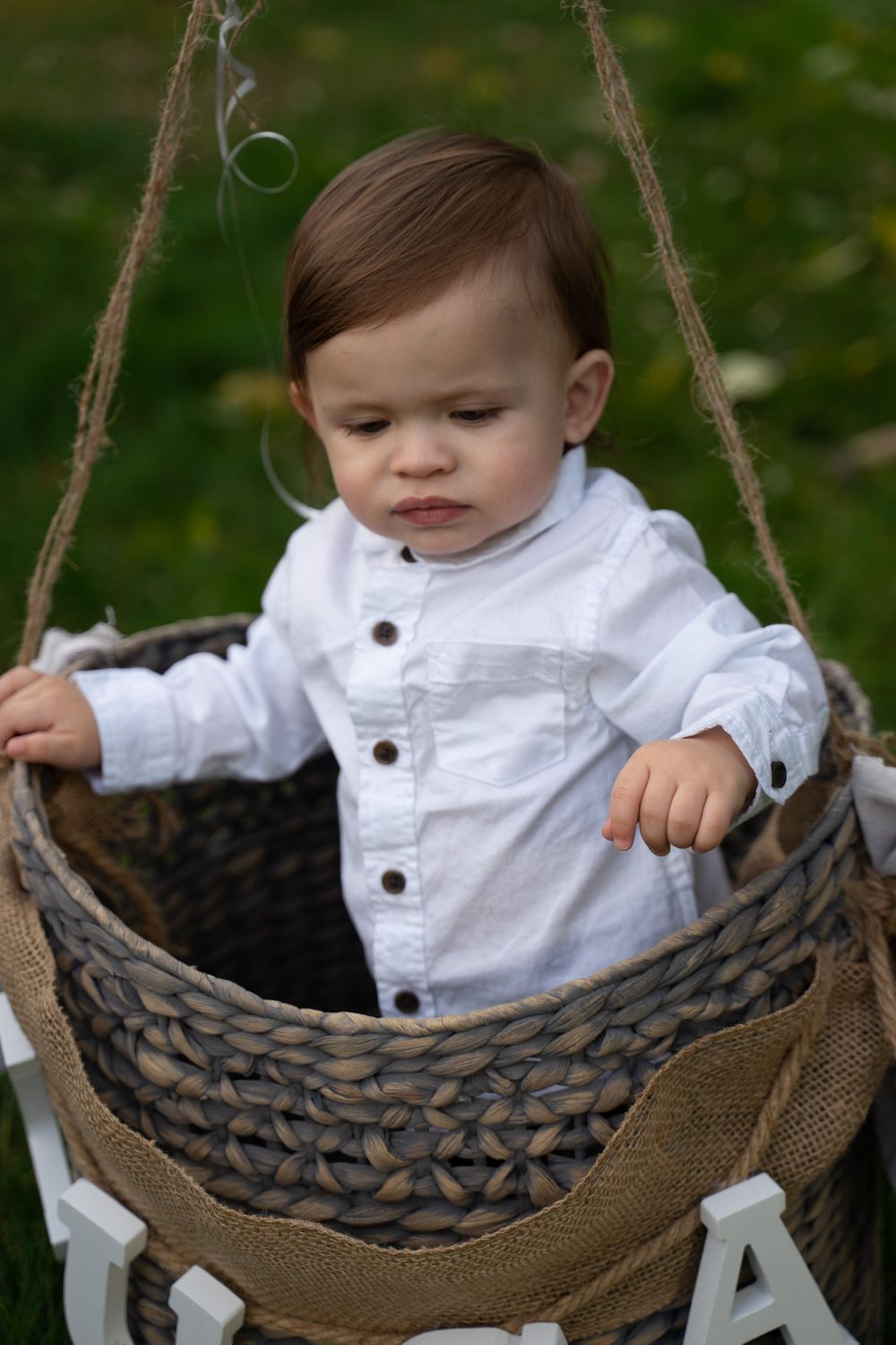 Rustic woven basket swing decorated with letters in an outdoor garden setting.