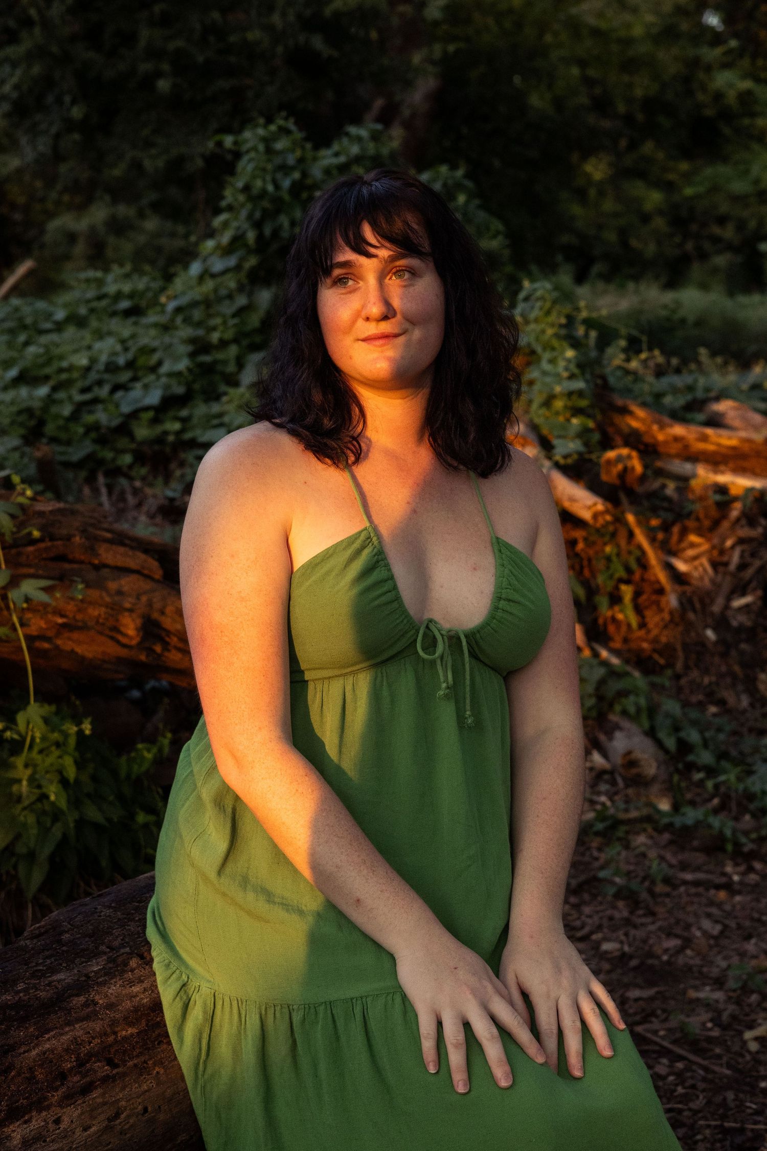 Woman sits in the forest lit dramatically by a sunray.