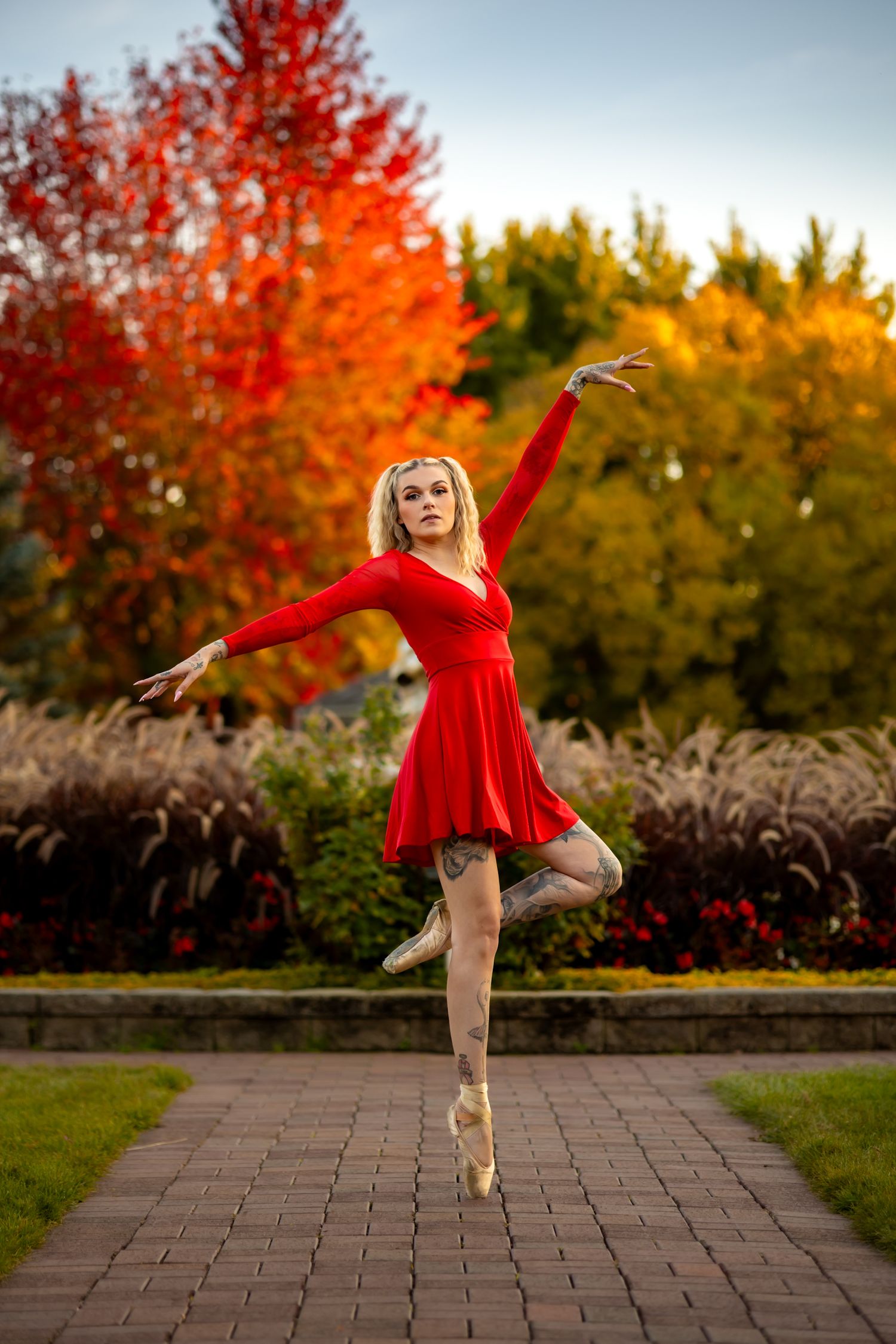 Ballerina in red dress performs en pointe pose against vibrant autumn foliage.