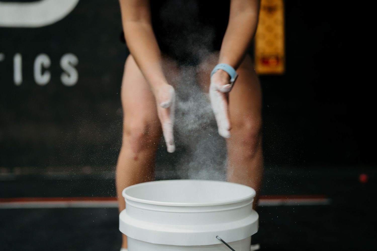 Chalk dust billowing from hands over a white bucket in a fitness environment.
