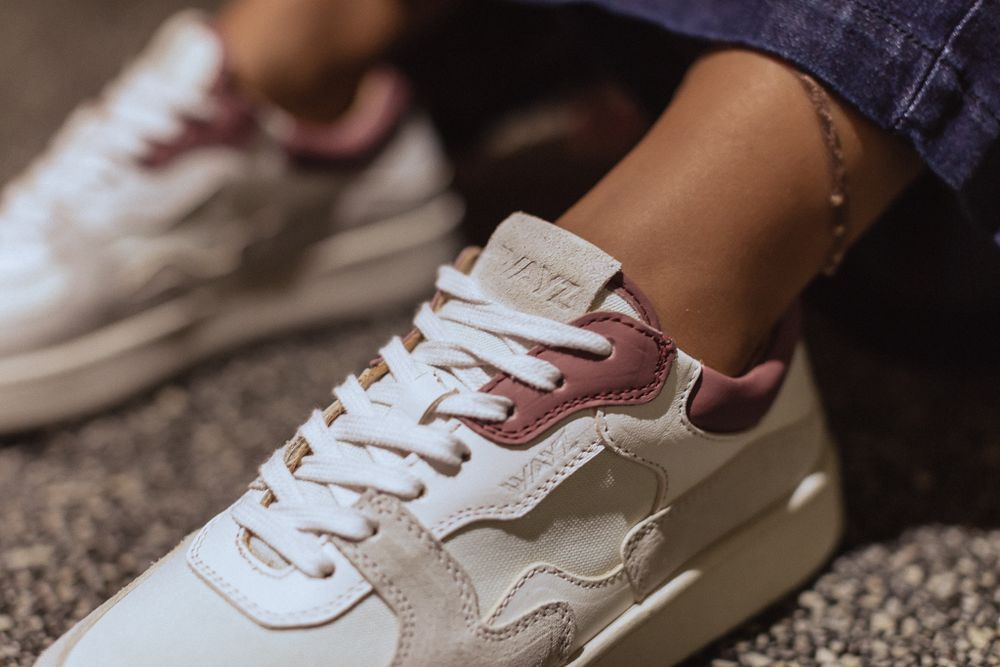 Close-up of a pair of white and rose gold sneakers on textured carpet.