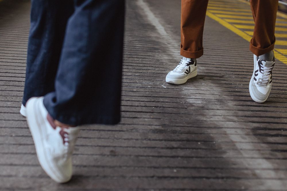 Close-up view of people wearing white sneakers and jeans standing on a wooden boardwalk surface.