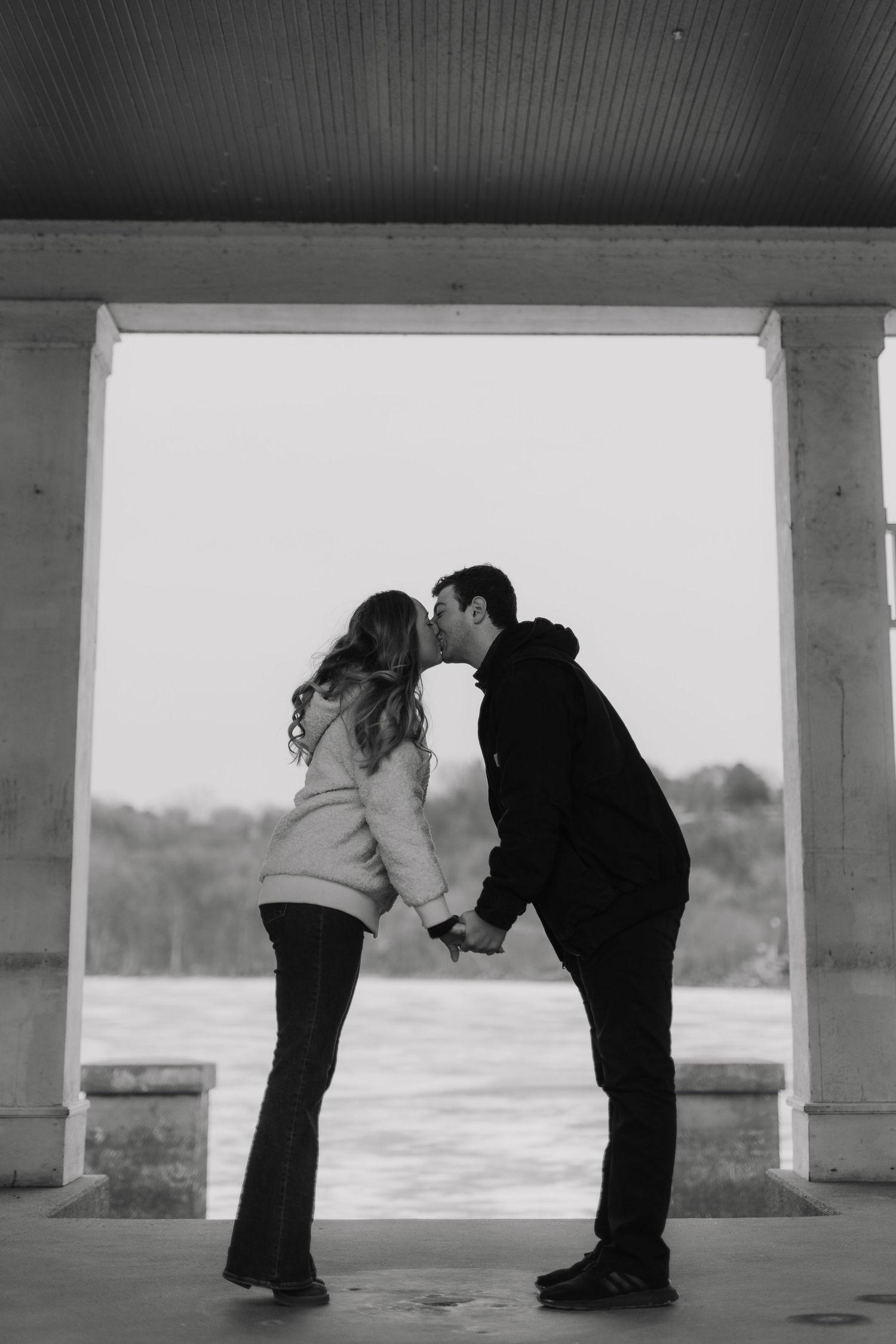 A romantic silhouette of a couple sharing a sweet kiss while standing in an outdoor covered walkway.