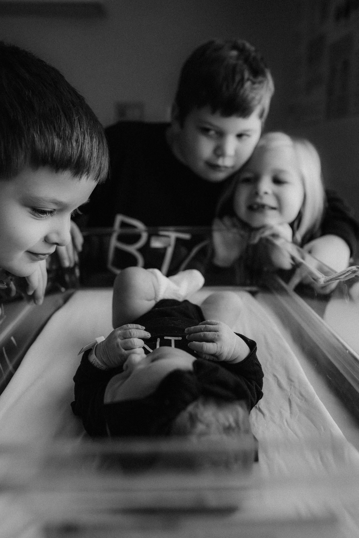 Black and white photo of siblings leaning over a table looking at something together with joyful expressions.