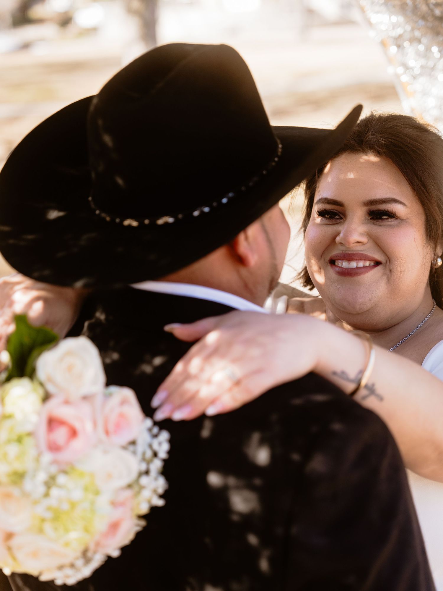 A happy couple shares a joyful moment at their western-themed wedding celebration with soft pink floral bouquet.