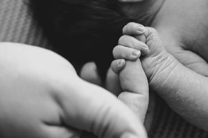 Black and white photo of a newborn baby grasping an adult's finger, symbolizing new life and parental bond.