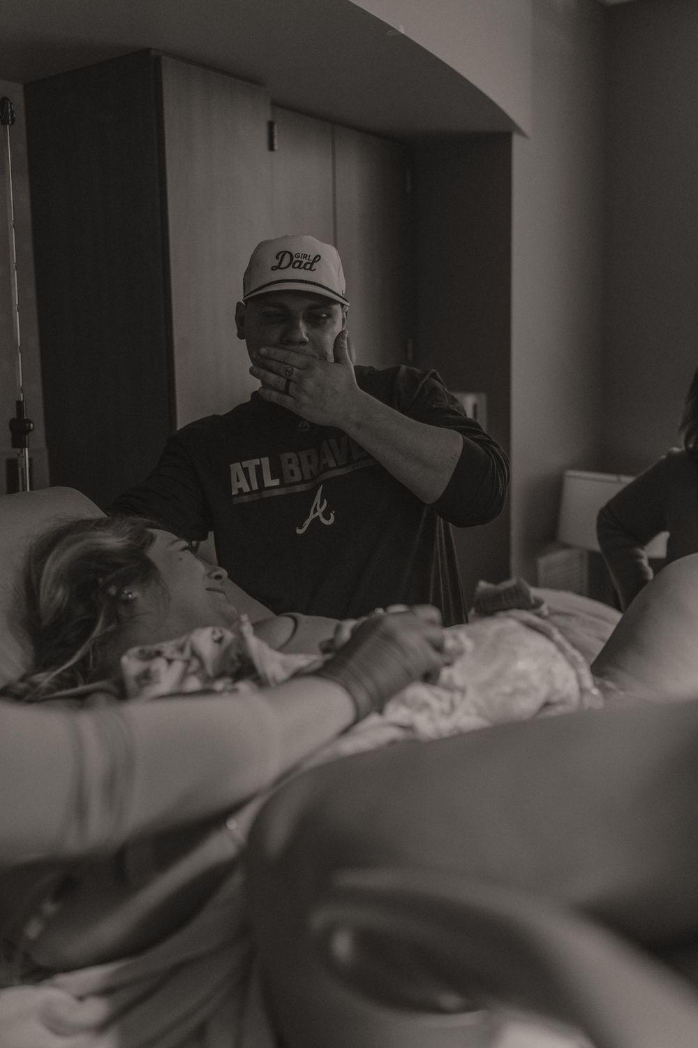 Hospital room with baseball cap wearing visitor beside bed.