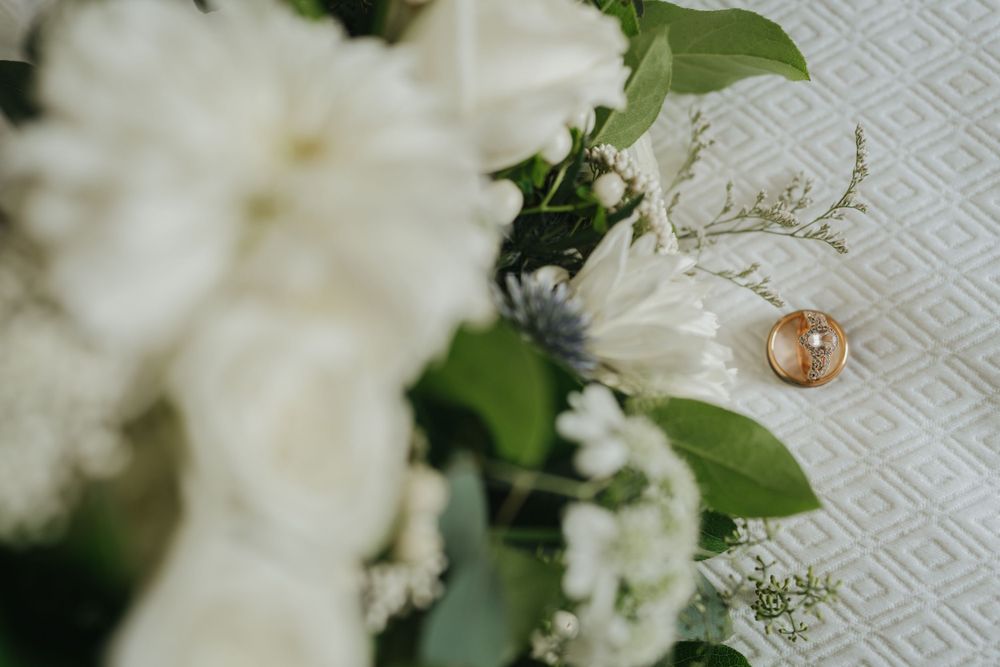 White flowers and wedding ring arranged on textured fabric.