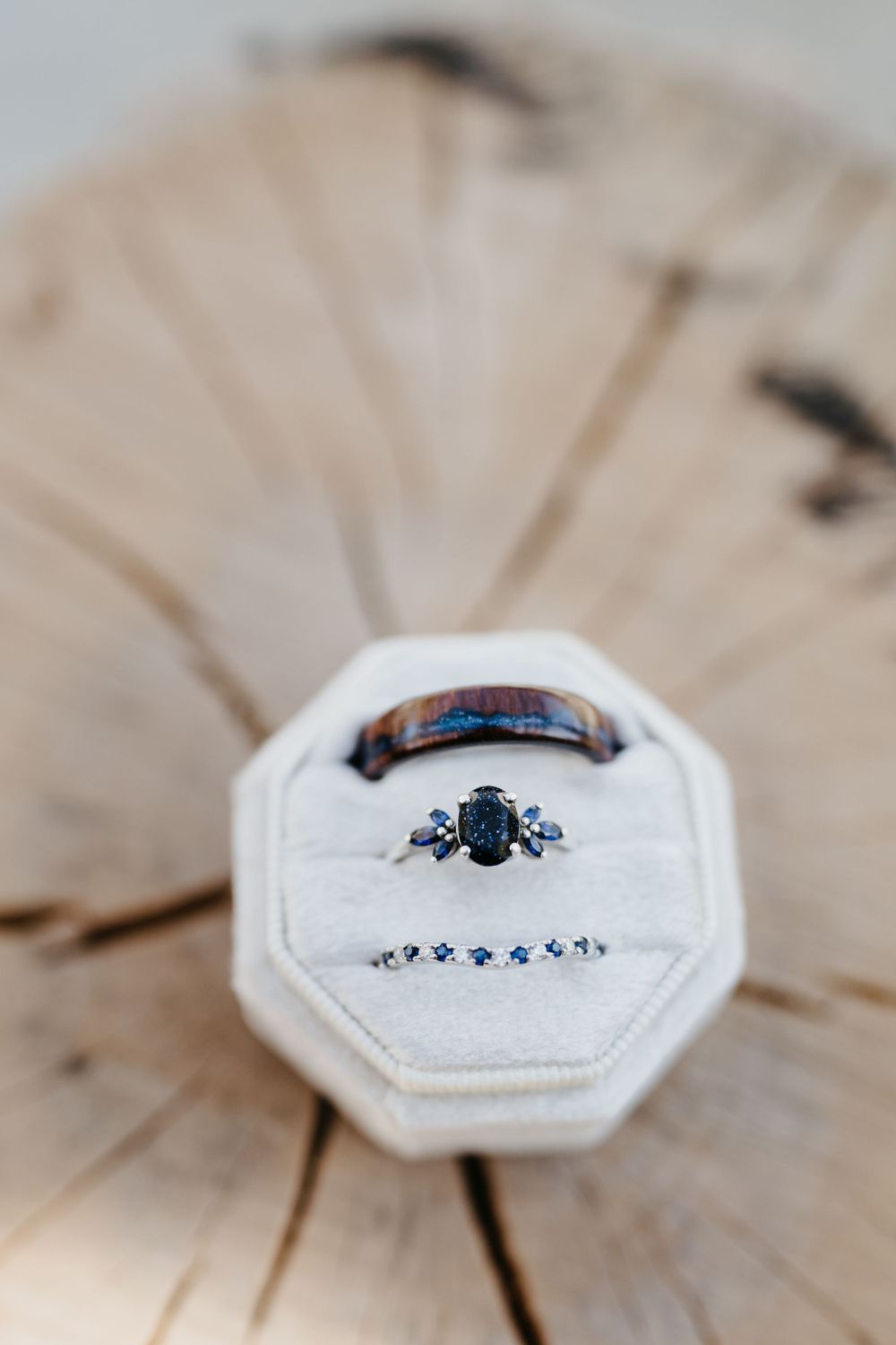 Elegant engagement ring with blue sapphire stone and wedding band displayed in white octagonal ring box.