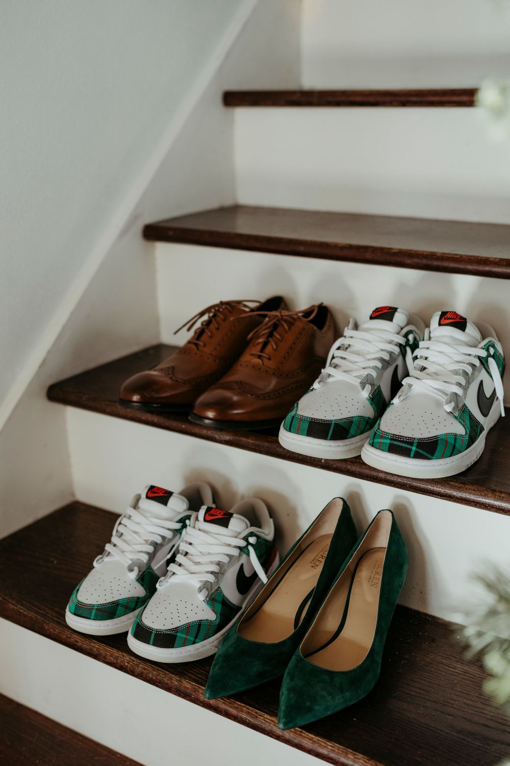 Various shoes including brown leather boots, white sneakers with green accents, and green heels arranged on wooden stairs.