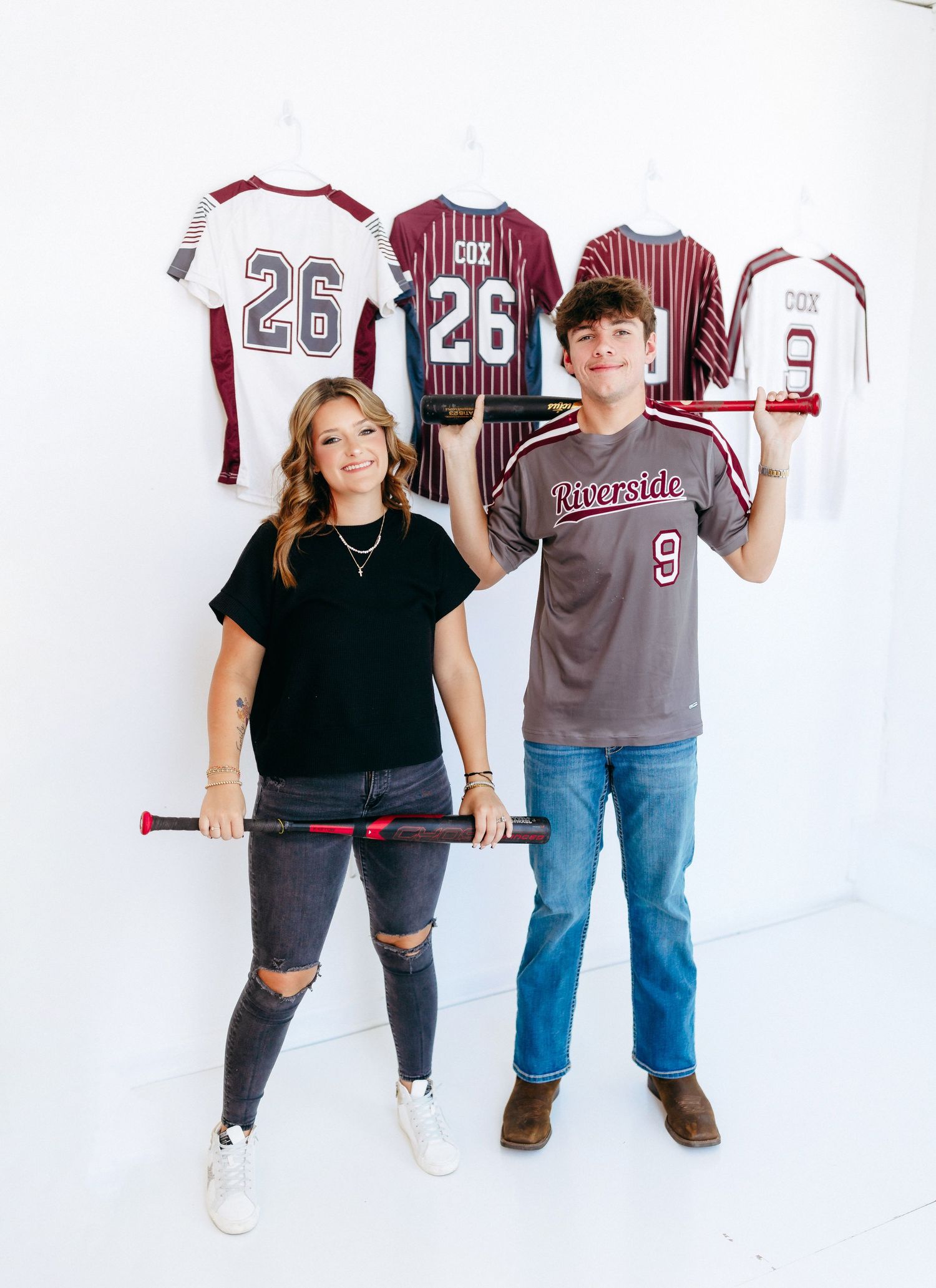 Two people stand against a white wall displaying baseball jerseys with matching numbers and striped patterns.