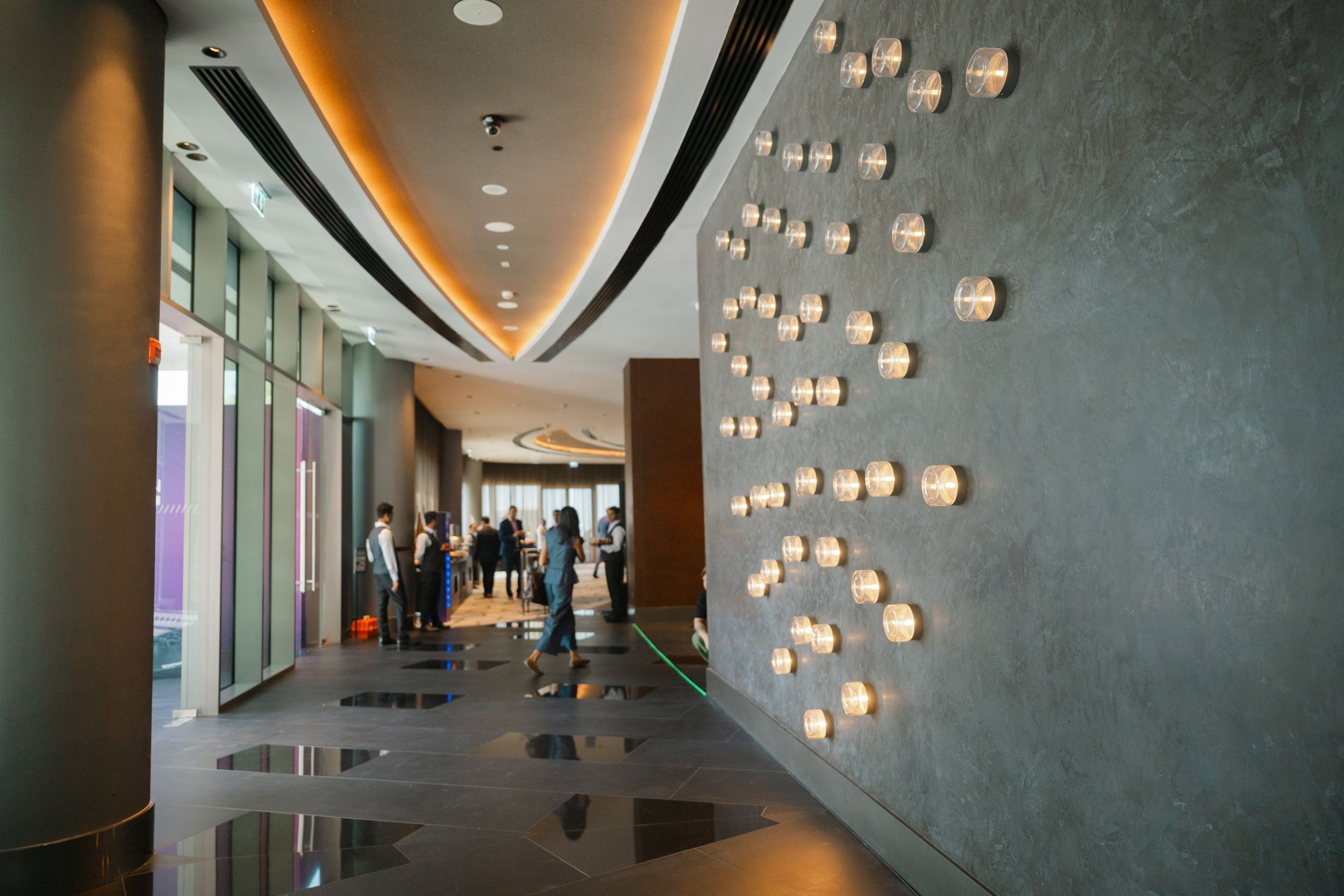 Modern office hallway with curved walls, pendant lights, and people walking in the distance.