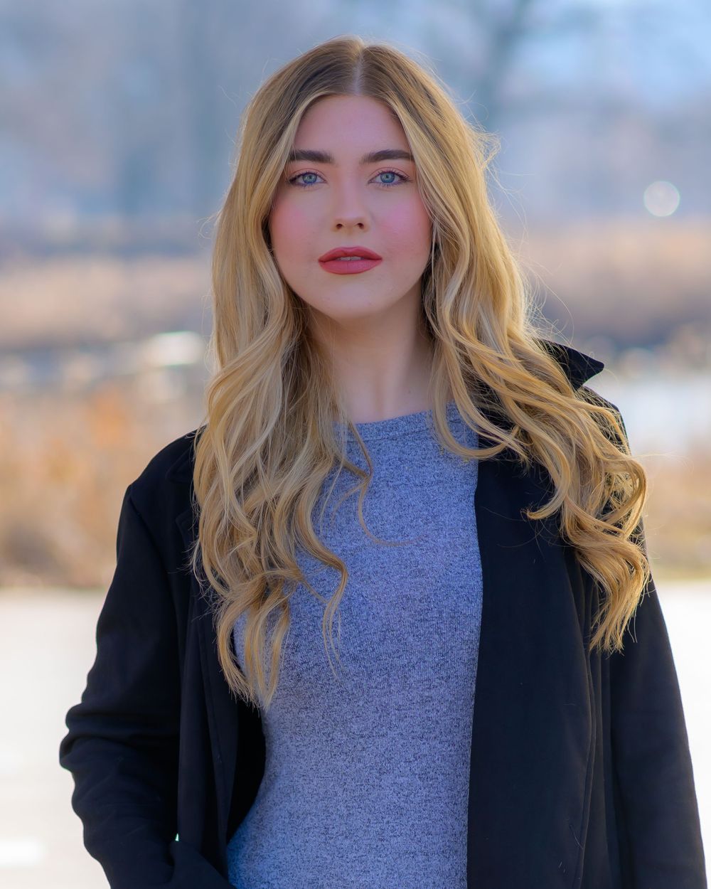 Winter fashion portrait showcasing a black coat and grey sweater with wavy blonde hair.