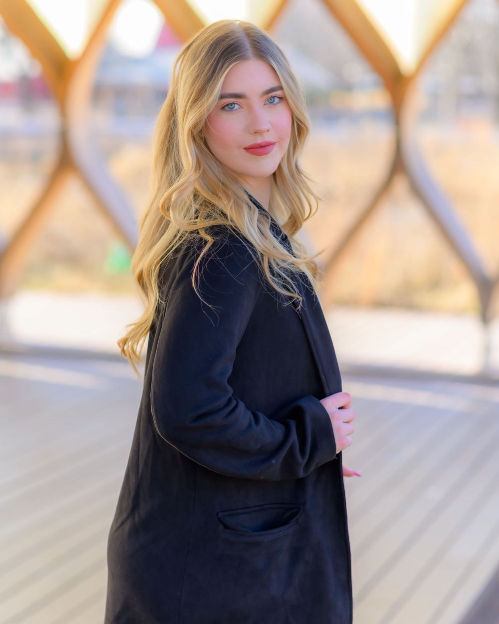 Stylish black coat ensemble photographed in front of a wooden lattice background.