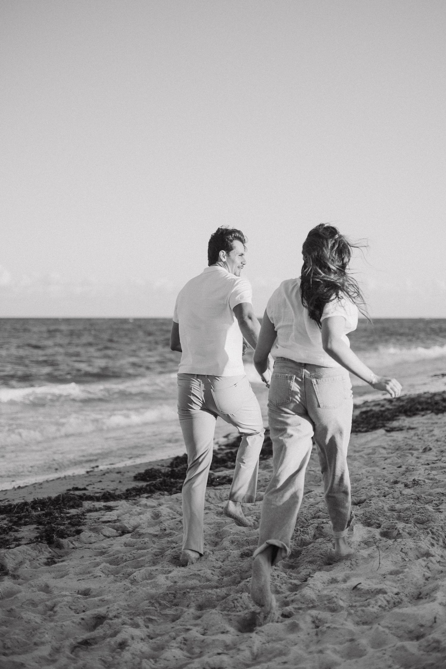 Black and White image of couple running away from the camera on the beach in the sand