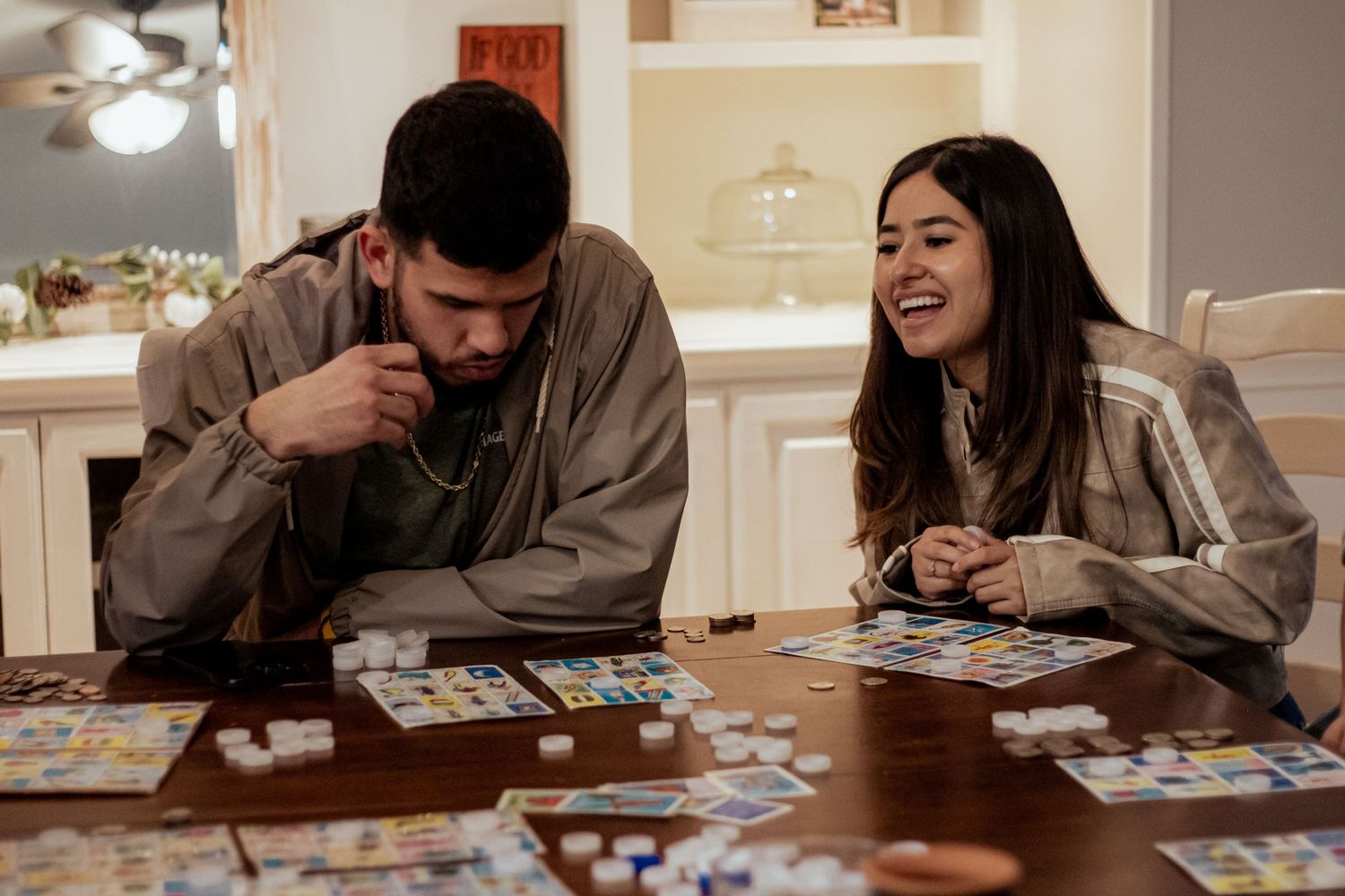 Two people sit at a table playing a card game together, laughing and enjoying a fun moment at home.