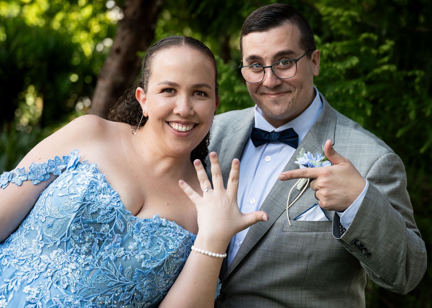 Couple showing off rings in formal attire outdoors during special occasion.