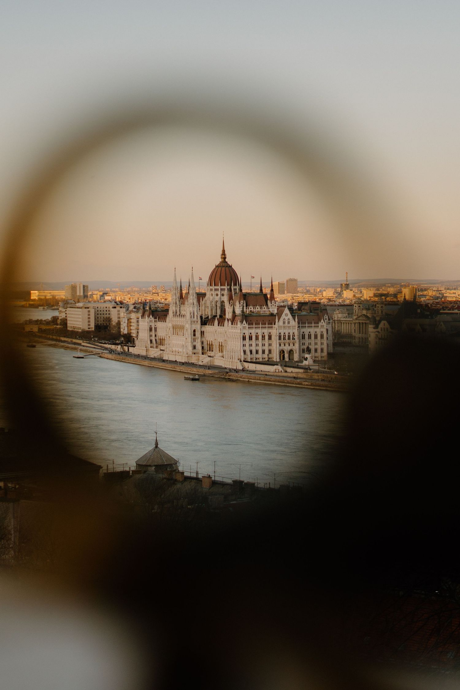 A moody view of Budapest's Parliament Building and Danube River at sunset through a circular vignette frame.