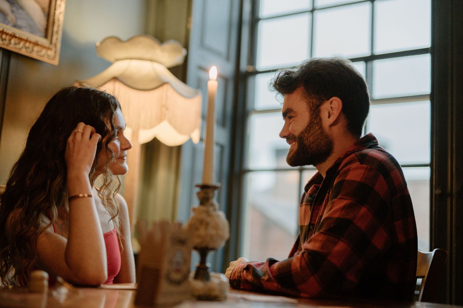 Two people share a heartfelt conversation while sitting together at a table under warm lighting in a cozy interior setting.