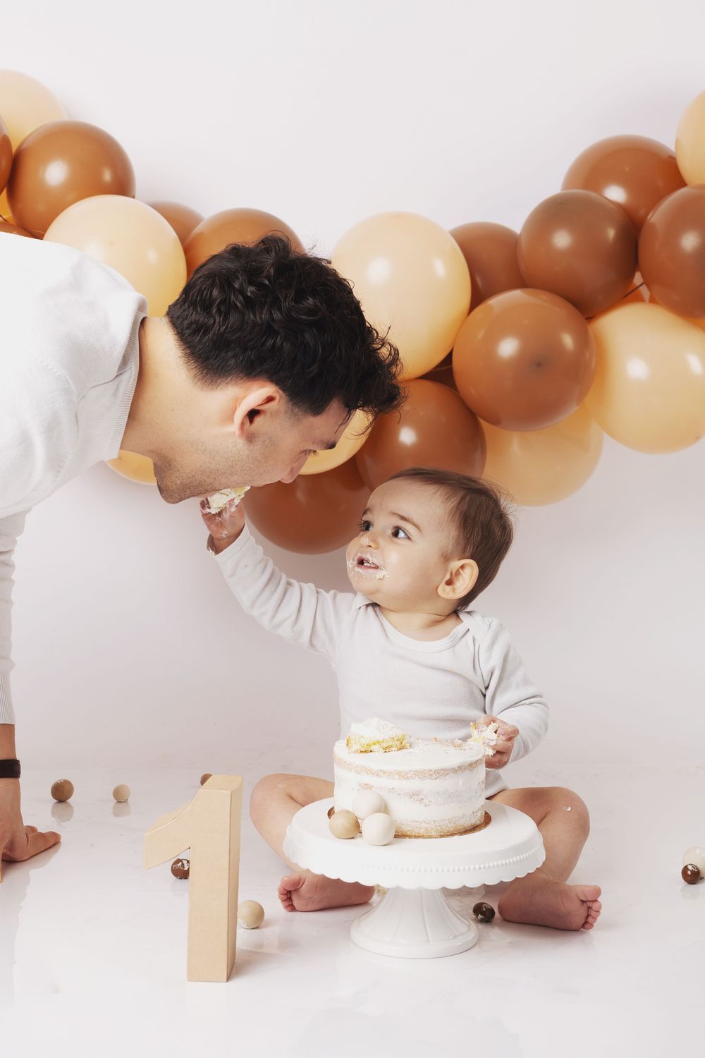 A sweet moment captured with balloons in earth tones as decorative backdrop during a cake smash photo session.