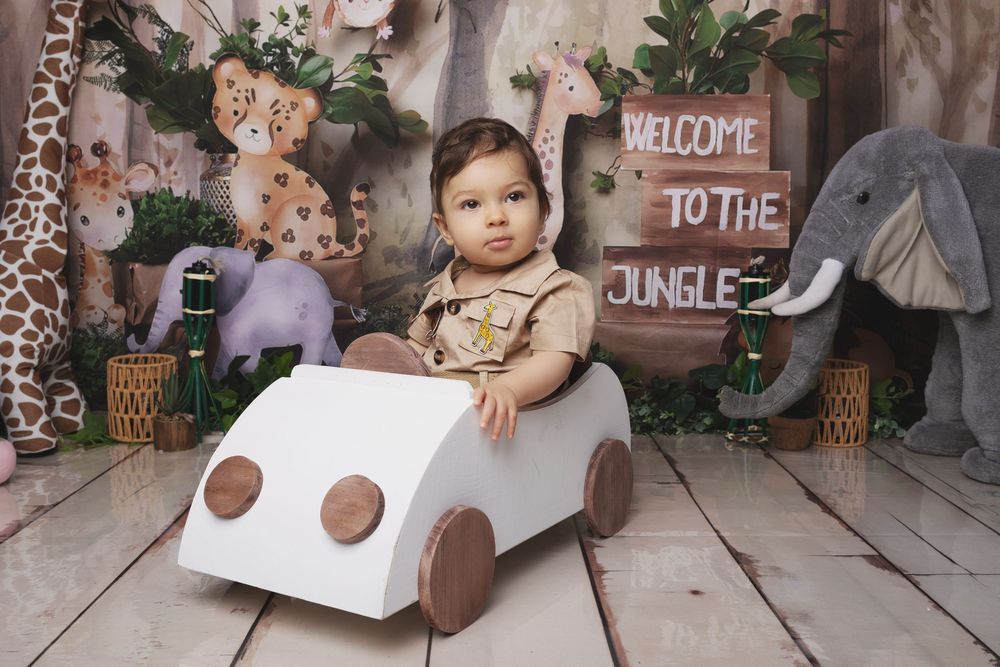 Safari-themed first birthday party setup with wooden decorations, greenery, and a 'Welcome to the Jungle' sign.
