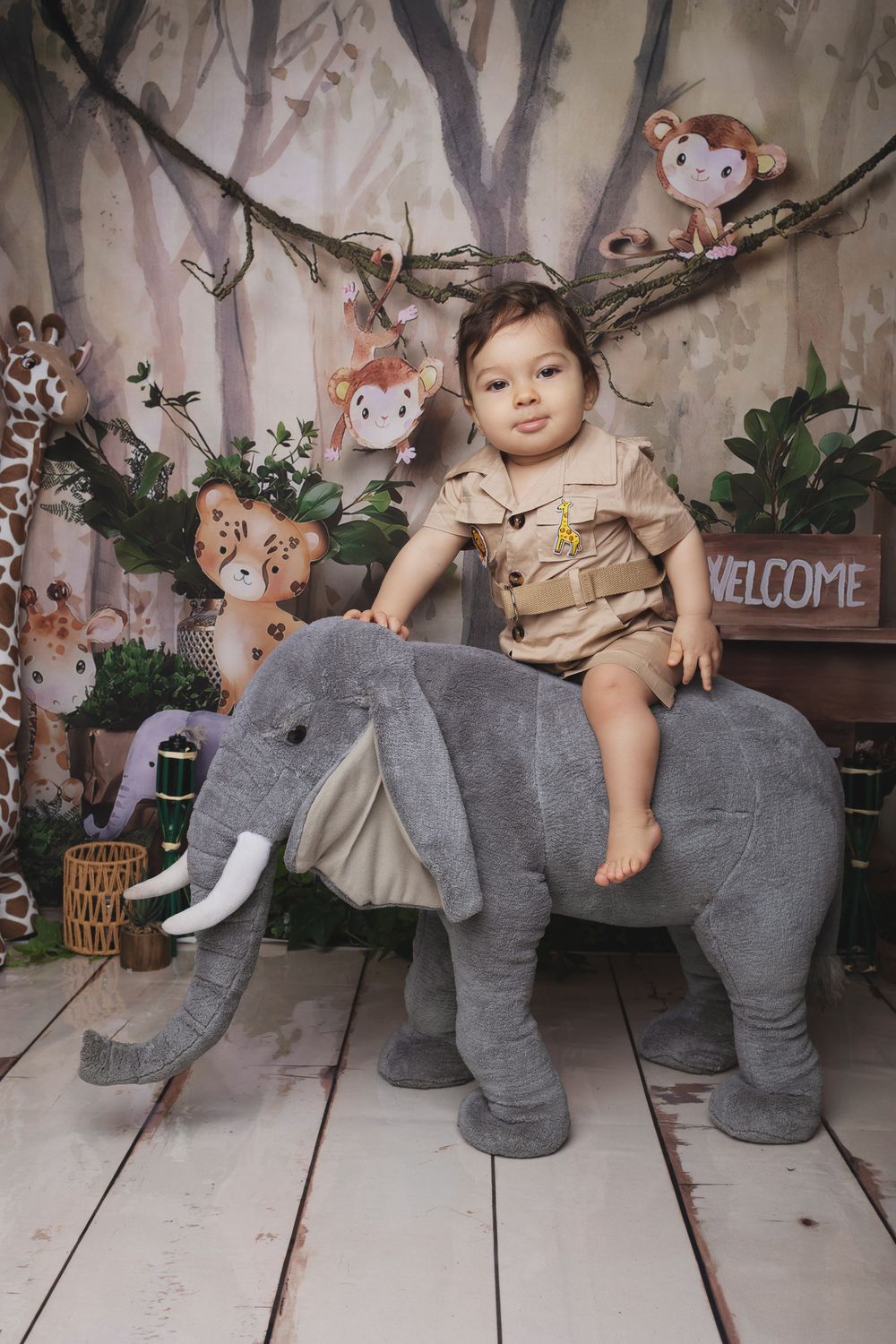 A child poses with a large plush elephant toy in a whimsical woodland-themed photo studio setting.